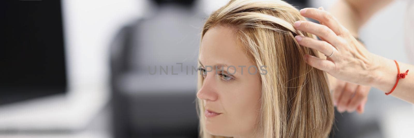 Portrait of female client on appointment at hairdresser, professional master creating haircut, touching hair. Beauty salon, hair treatment, wellness, new image, change life concept. Blurred background