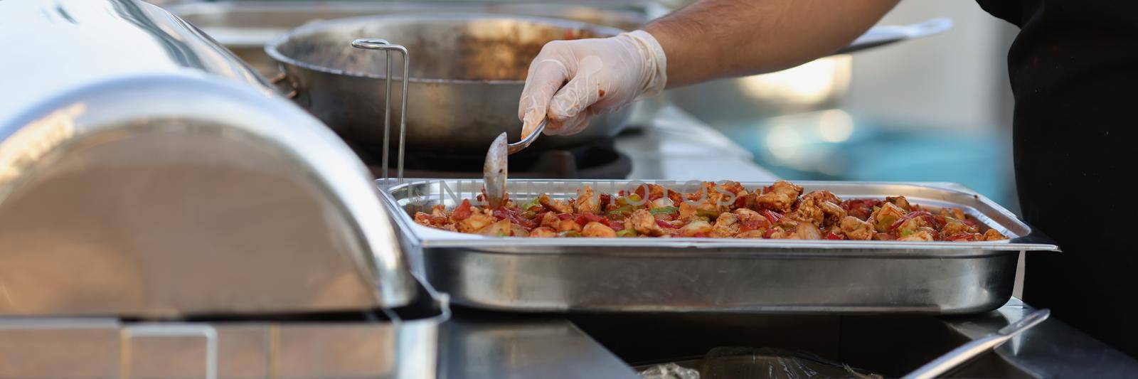 Close-up of street cooker preparing portion for sell. Big tray with fried chicken and vegetables in sauce, professional chef outdoors. Street food, takeaway, fast food, lunch concept