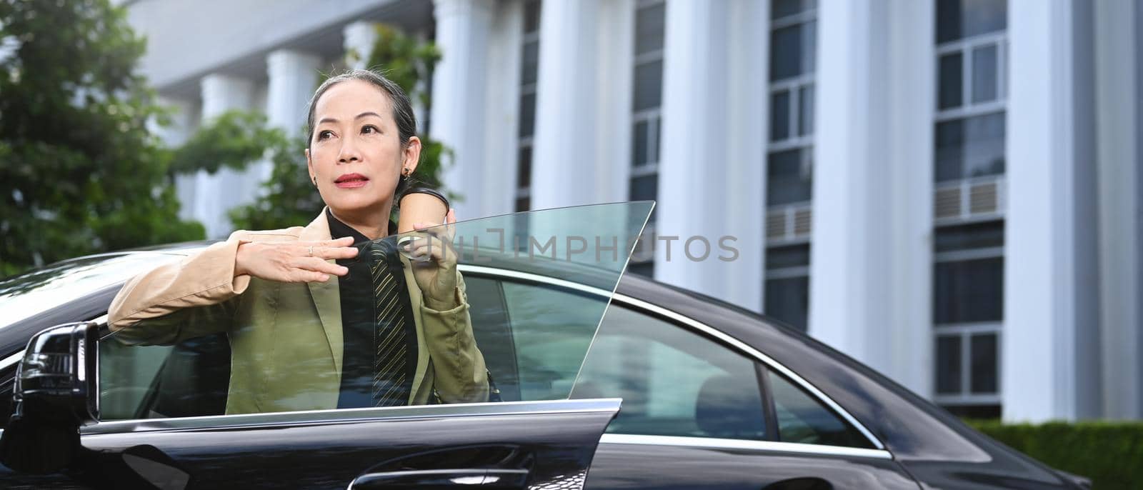 Elegant mature woman in business suit standing near a car on city street by prathanchorruangsak