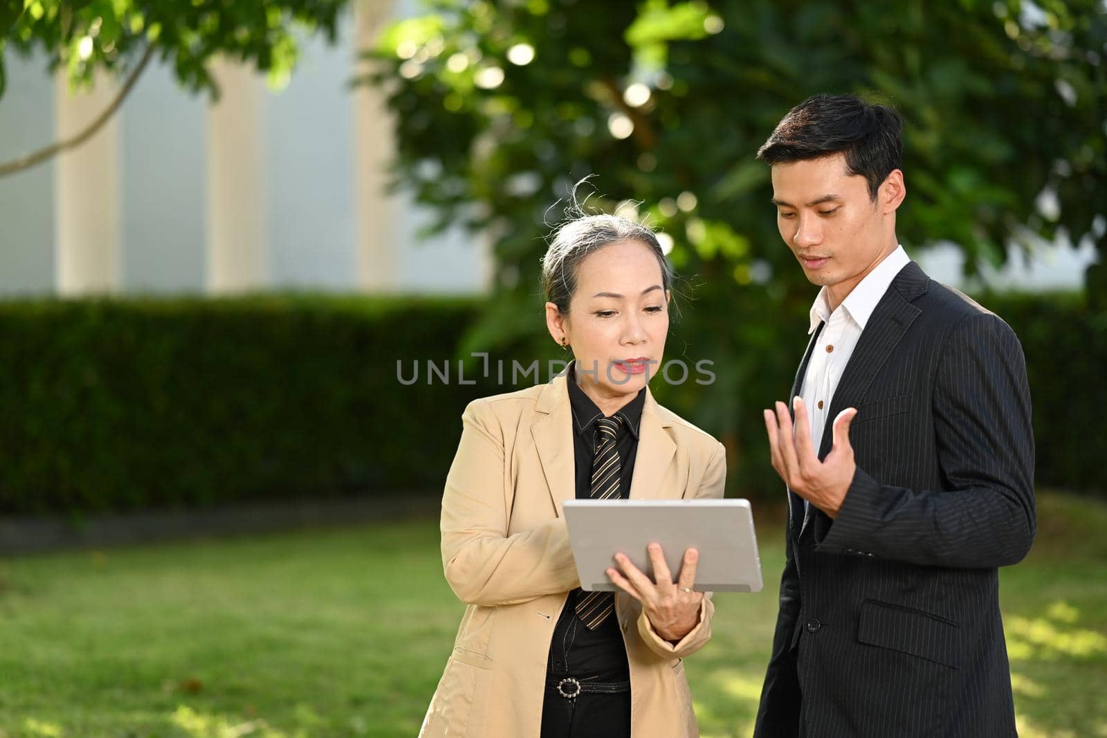 Successful business people in formalwear talking while walking on street in modern city by prathanchorruangsak