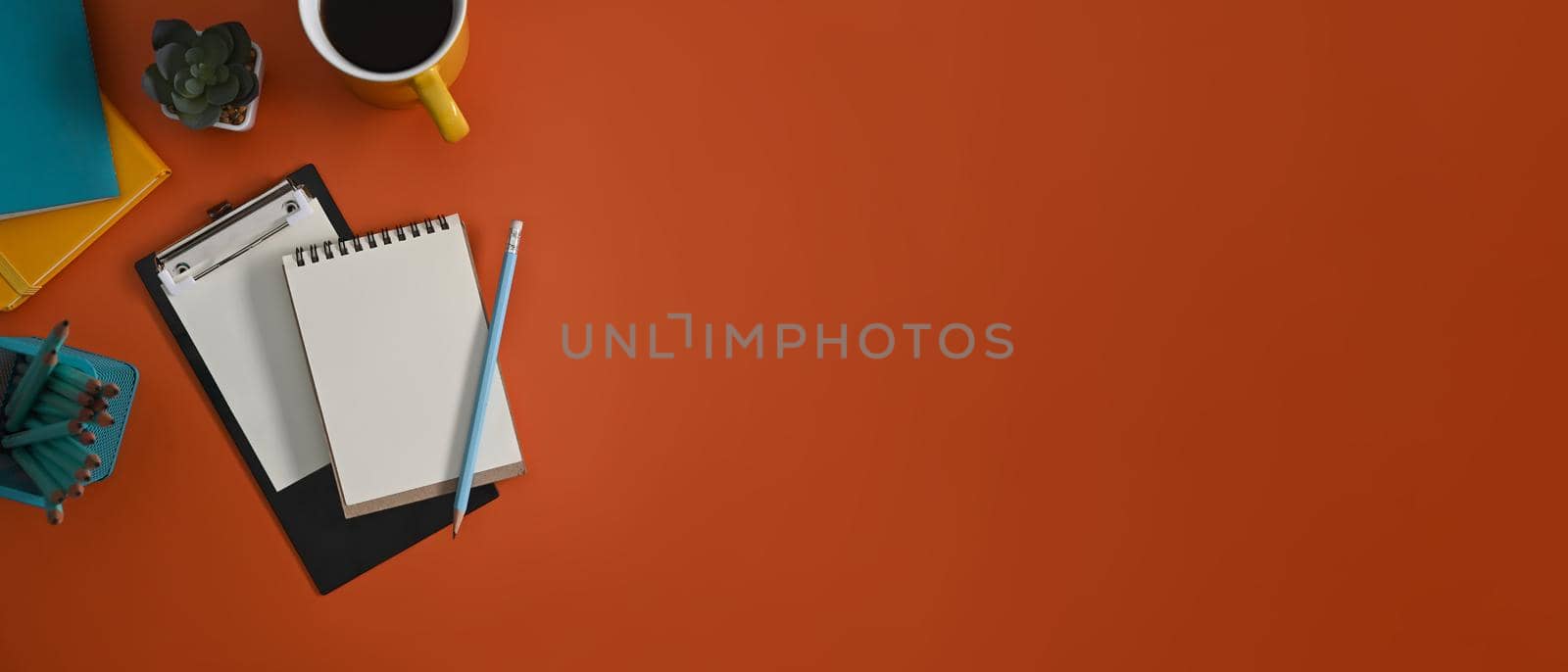 Top view notepad, clipboard, coffee cup and stationery on orange background with copy space.