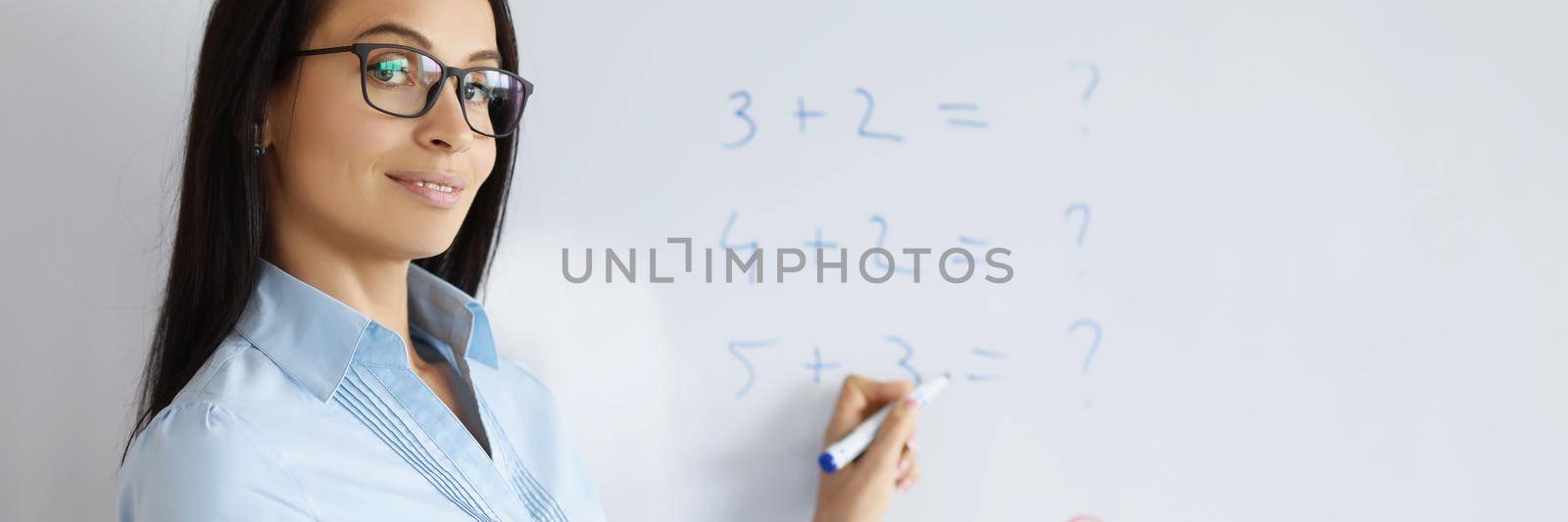 Portrait of young teacher at school explain maths to pupils. Examples with numbers on board, qualified professor. Copy space in right. Education, knowledge, school, university concept