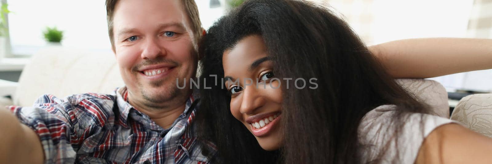 Portrait of friends taking selfie on sofa. Middle aged man and latinoamerican woman smiling for picture, warm friends meeting. Friendship, pastime, fun and happiness concept