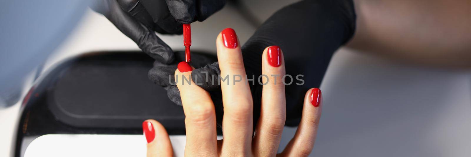 Close-up of manicure master using red varnish to cover clients nails. Fresh, trendy and bright nails after salon. Beauty treatment, manicure, nail care, wellness concept