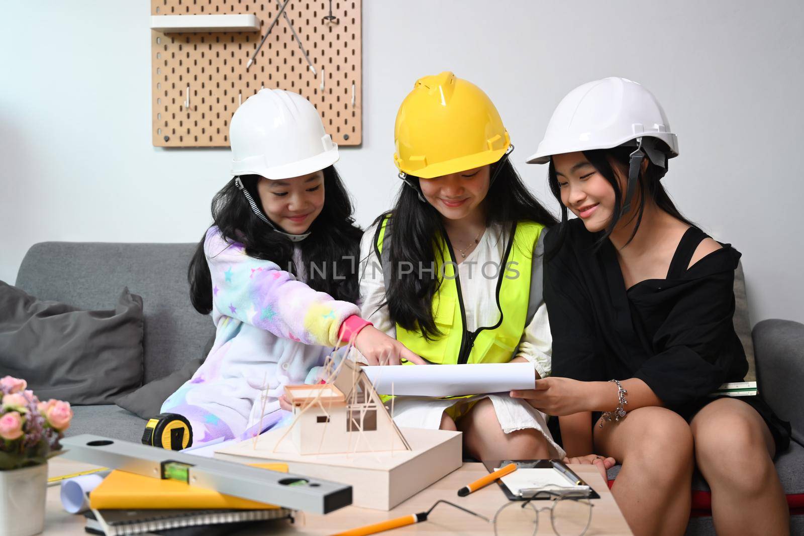 Three asian girls wearing safety helmet pretend to be engineer while playing together in living room. by prathanchorruangsak