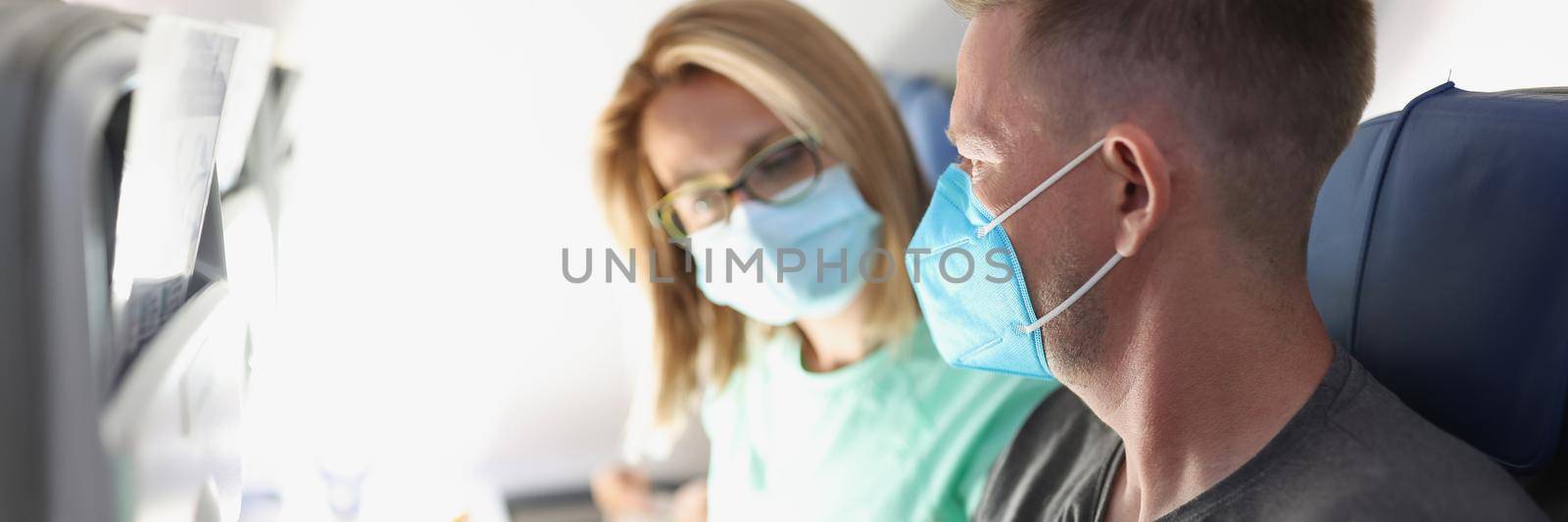 Portrait of family couple choosing meal on board. Hungry man discuss with wife food options, fly high in sky, wear face masks on flight. Airplane, food serving, menu, coronavirus, pandemic concept