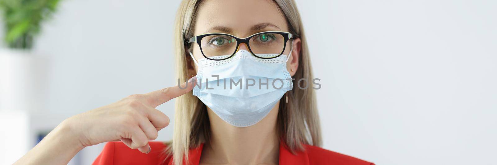 Portrait of businesswoman pointing at face mask with finger, importance of wearing protective equipment. Prevention of covid virus spread, protect yourself, social distance concept