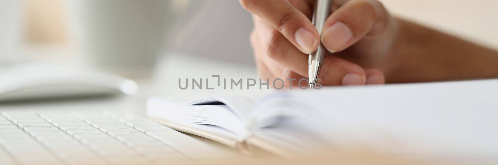 Close-up of person writing down ideas, impressions, making notes for future, planning day. Hand holding silver pen. Journaling, creativity, writer, thoughts concept. Blurred background