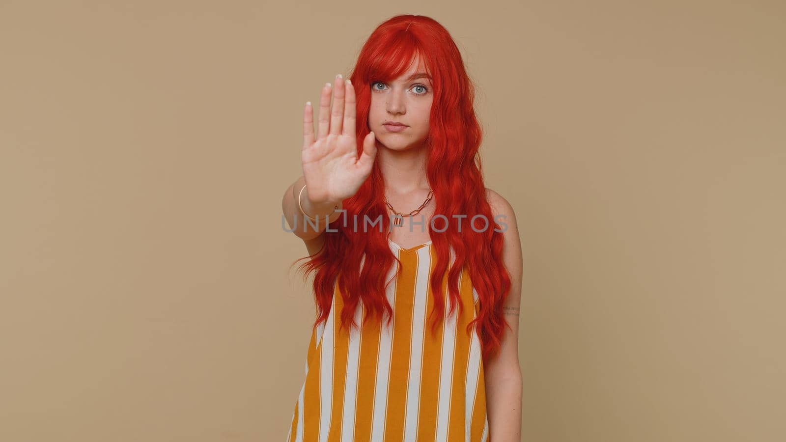 No stop. Serious woman say no, hold palm folded crossed hands in stop danger gesture, warning of finish, prohibited access, declining communication, body language. Redhead one girl on beige background