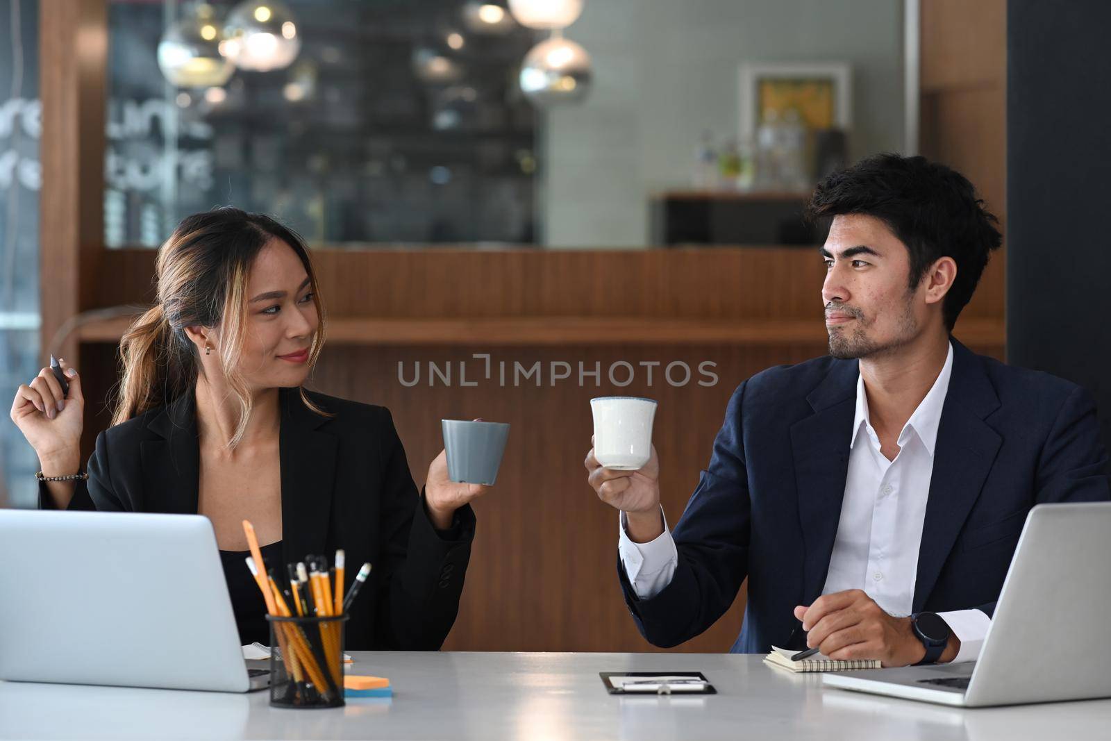 Two young managers drinking coffee and chatting during break at bright office.