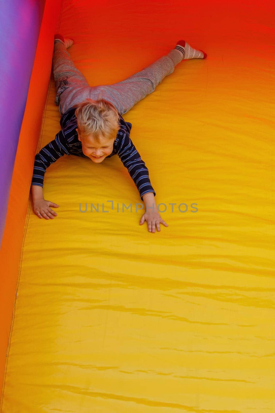 Little boy is actively playing on a children's inflatable trampoline. He slides down on his stomach. Bright red-yellow colors. Free copy space. by Lincikas