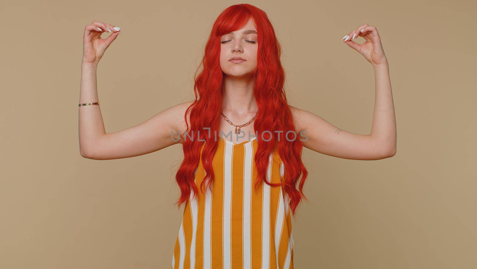 Keep calm down, relax, inner balance. Woman breathes deeply with mudra gesture, eyes closed meditating with concentrated thoughts, peaceful mind. Redhead adult girl isolated on beige studio background