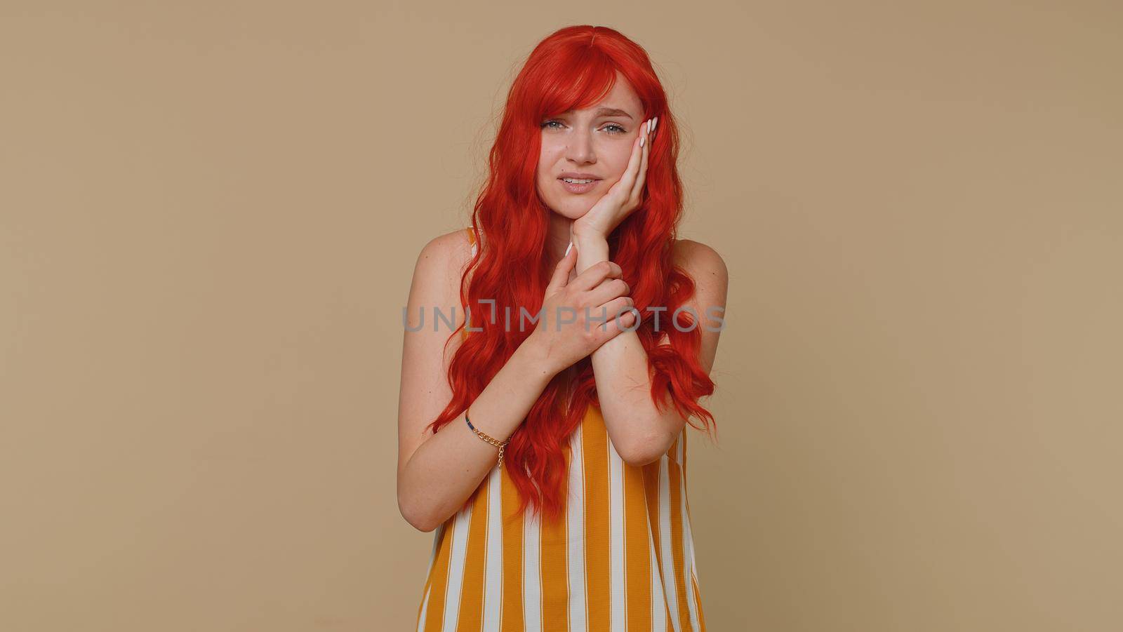 Redhead young woman touching sore cheek suffering from toothache cavities or gingivitis waiting for dentist appointment gums disease. Ginger girl indoors studio shot isolated alone on beige background