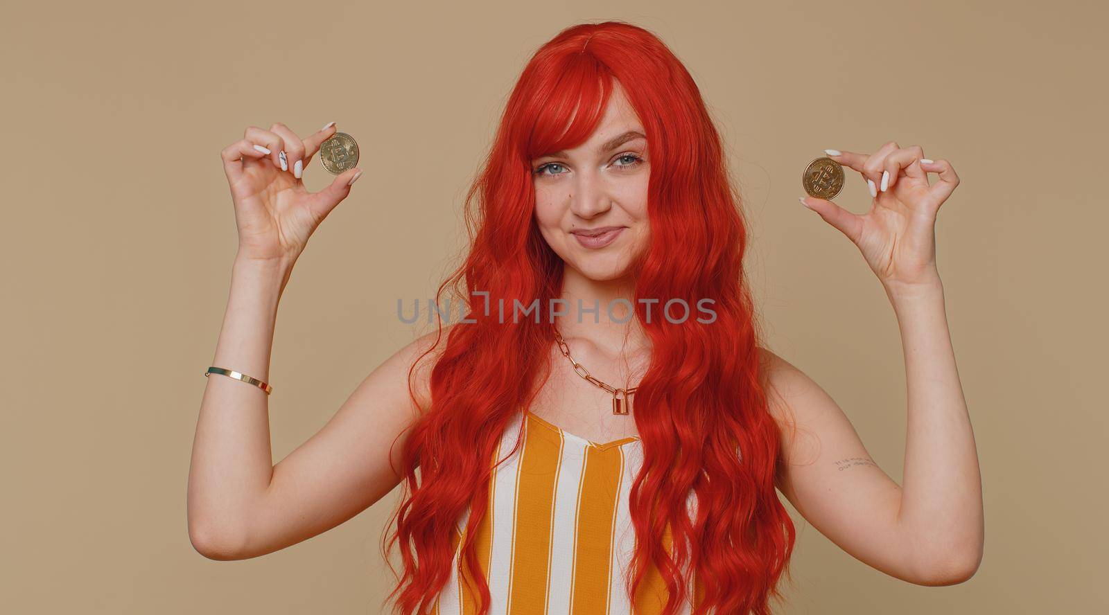 Redhead woman winner showing golden bitcoins. Career wealth cryptocurrency investment mining future technology. Young ginger girl fooling making faces. Happy businesswoman isolated on beige background
