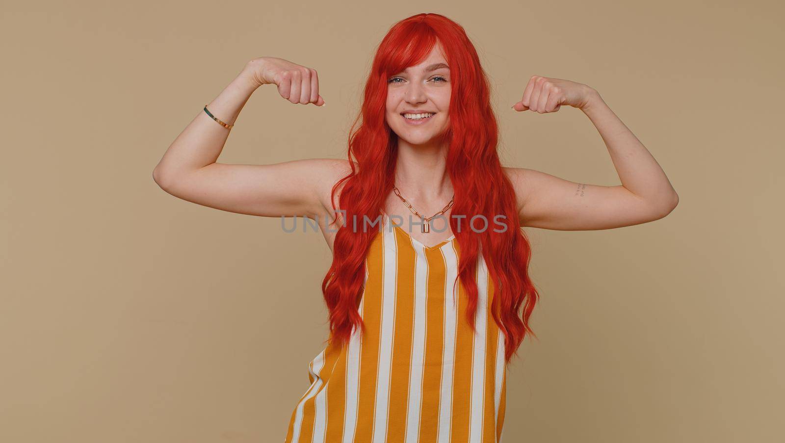 I am strong and independent. Redhead woman showing biceps, looking confident, feeling power strength to fight for rights, energy to gain success win. Ginger girl isolated on beige studio background