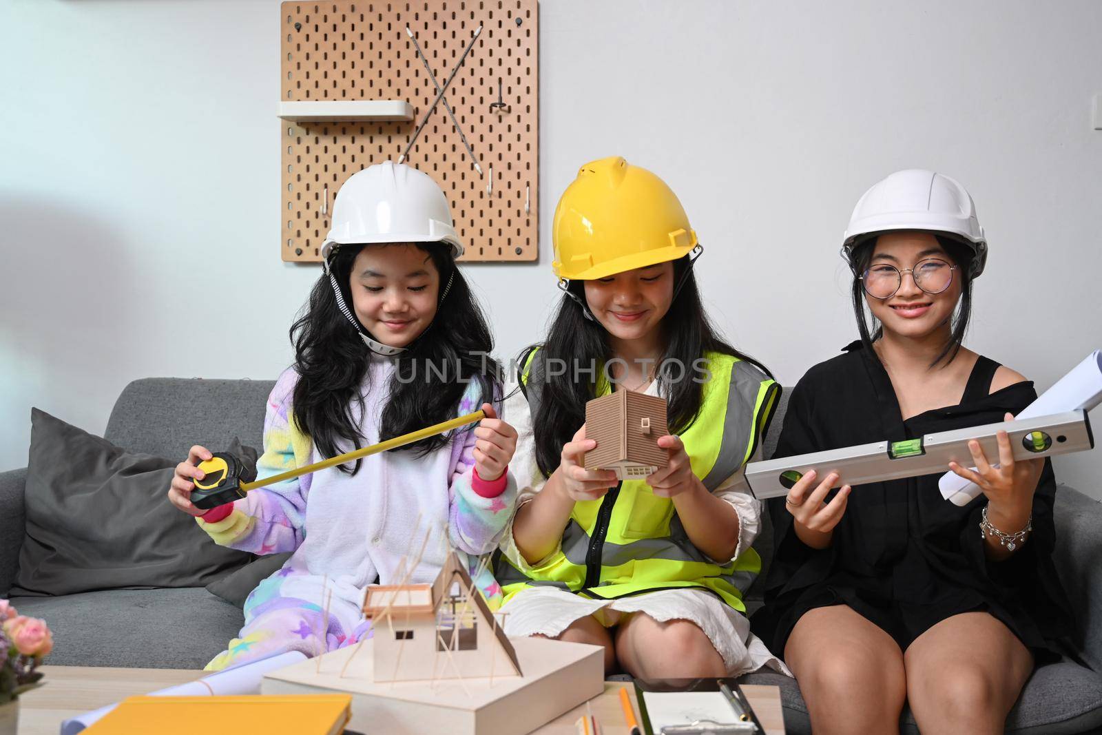 Three lovely asian girls wearing safety helmet pretend to be engineer while playing together at home. by prathanchorruangsak