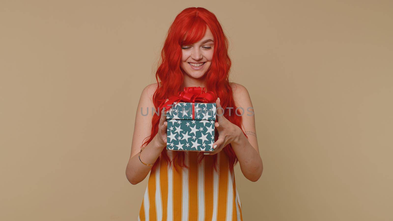 Cheerful red hair young winner woman receive gift box, birthday surprise and expressing great happiness amazement, satisfied with best present bonus. Ginger girl isolated on beige studio background