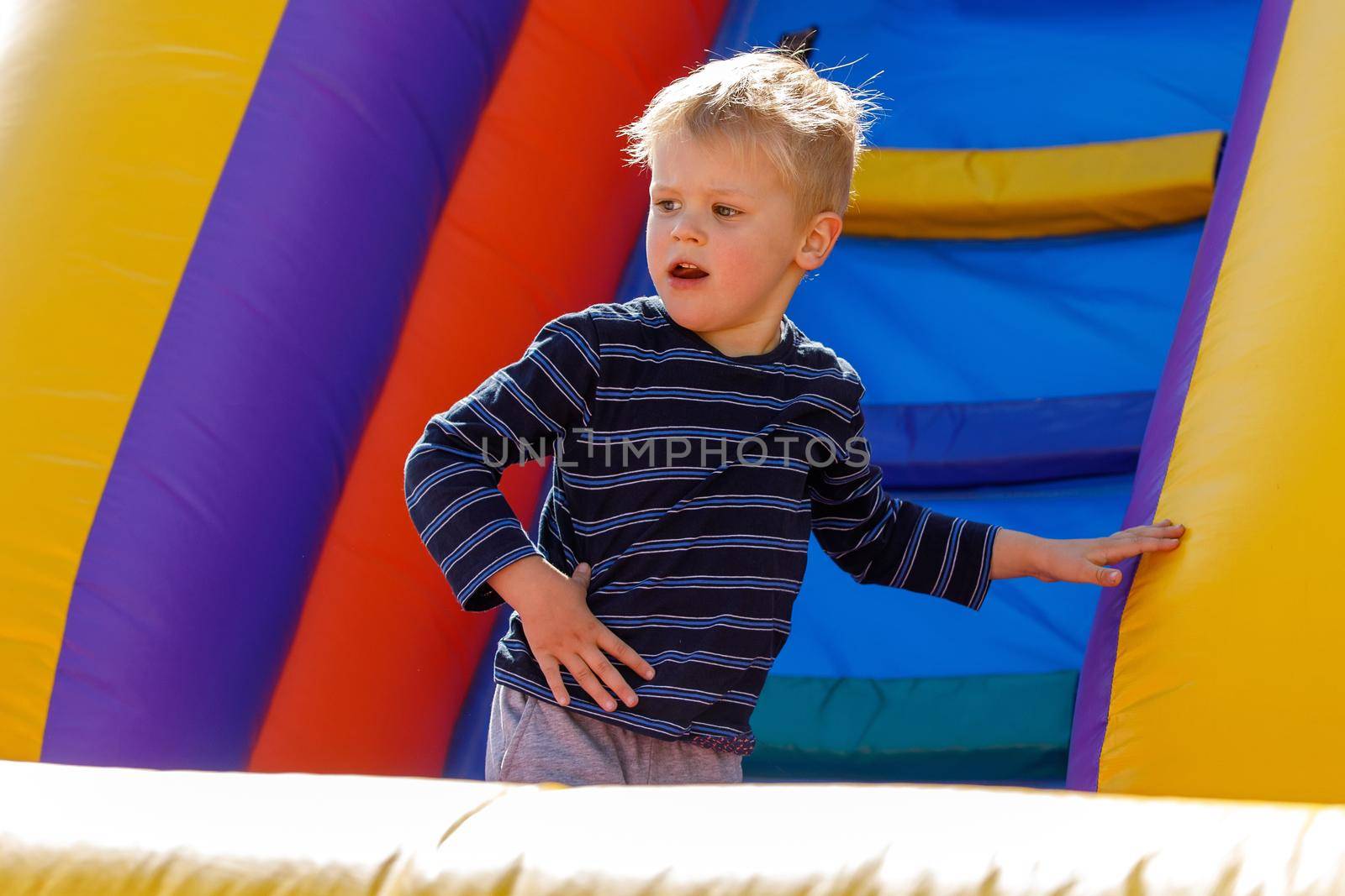 Child jumping on colorful playground trampoline. Kid jump in inflatable bounce castle on kindergarten birthday party. Activity and play center for young child. Little boy playing outdoors in summer.