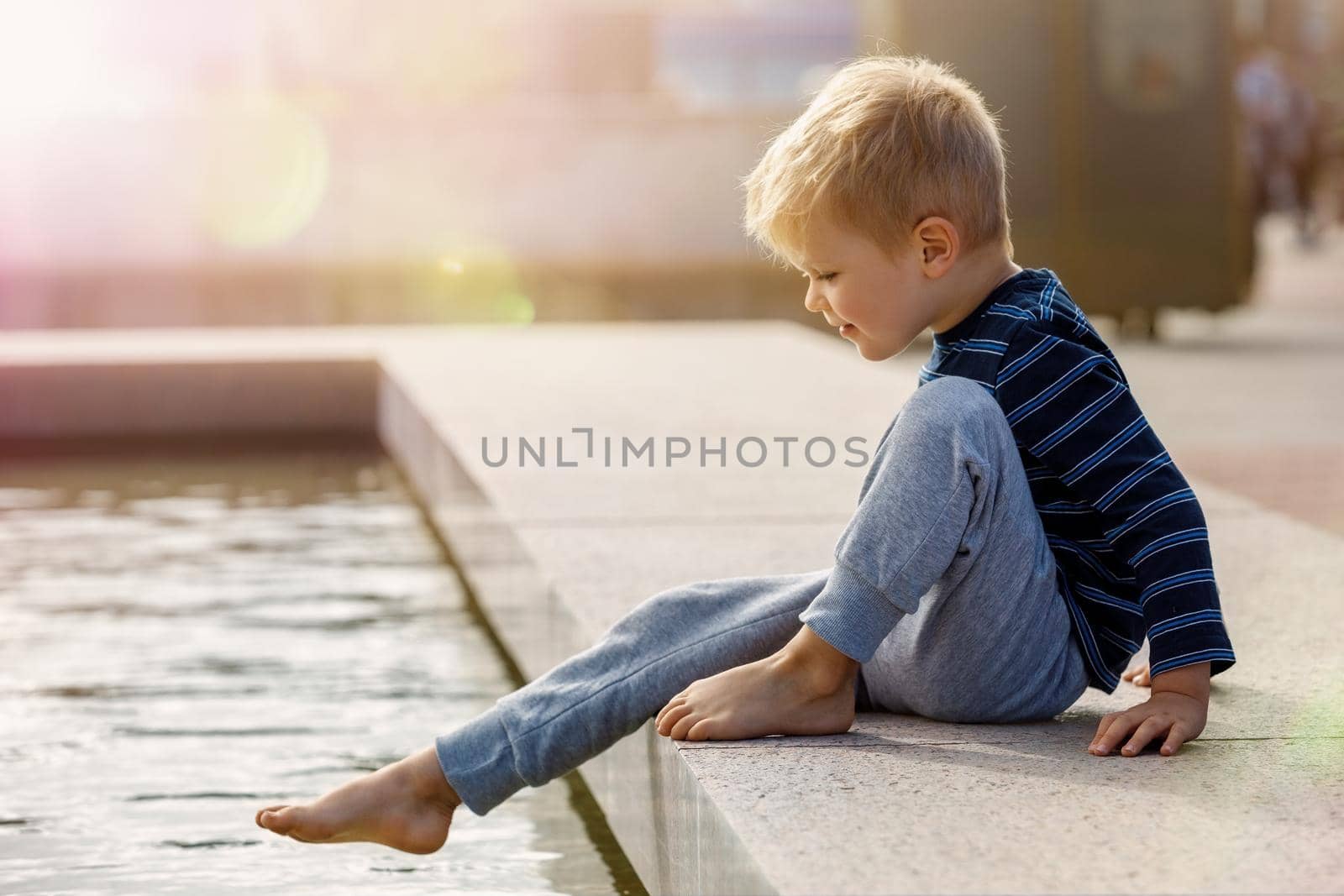 A cute little boy, barefoot, wants to climb into the water at the city fountain during the summer.