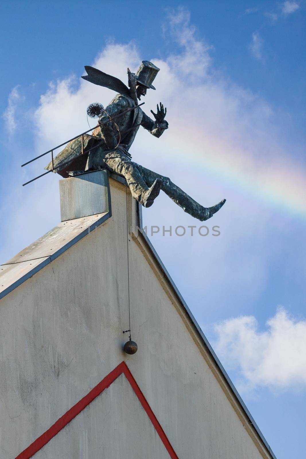 Chimney Sweeper Sculpture on roof in old town of Klaipeda, Lithuania. House wall in Klaipeda Old Town. Blue sky with white clouds and rainbow. by Lincikas