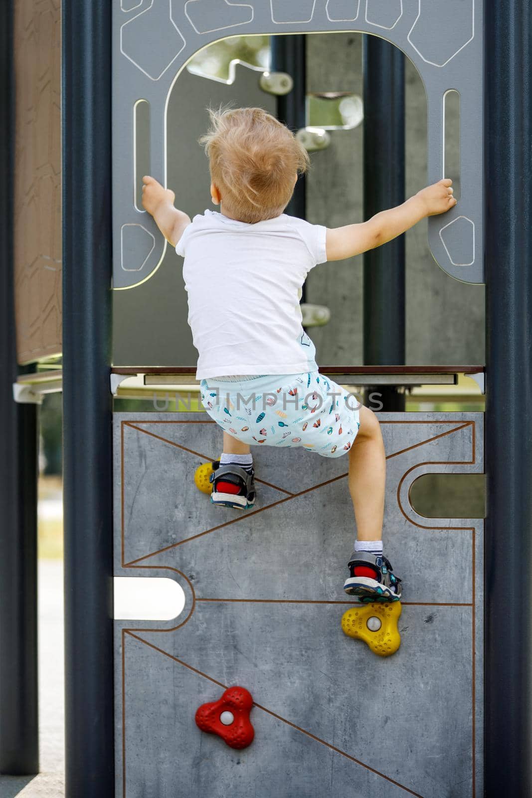 A young mountaineer trains to climb the climbing wall. Active child time spending concept image.