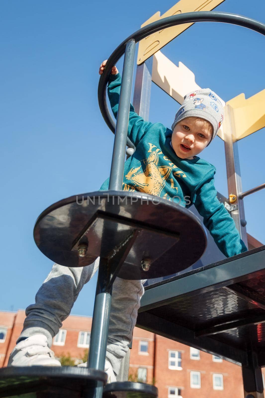 A careful little boy climbs up the playground equipment, view from below, against a background of blue sky.