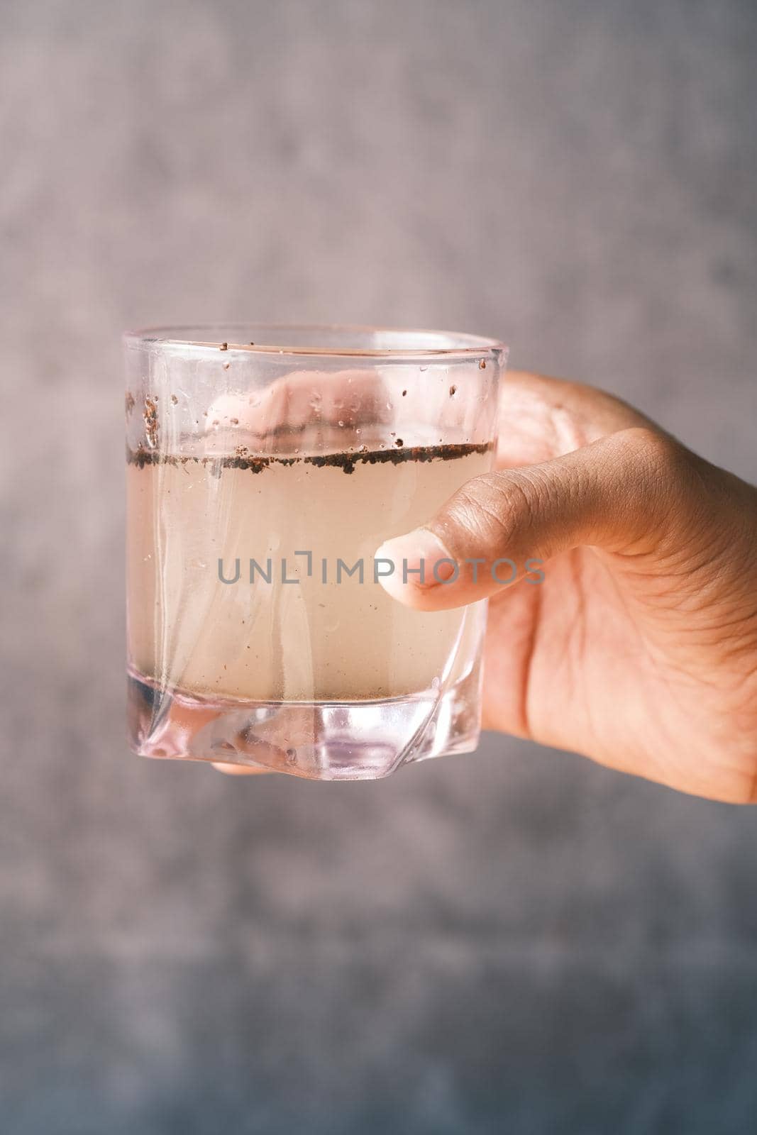 holding dirty glass of water against black background .
