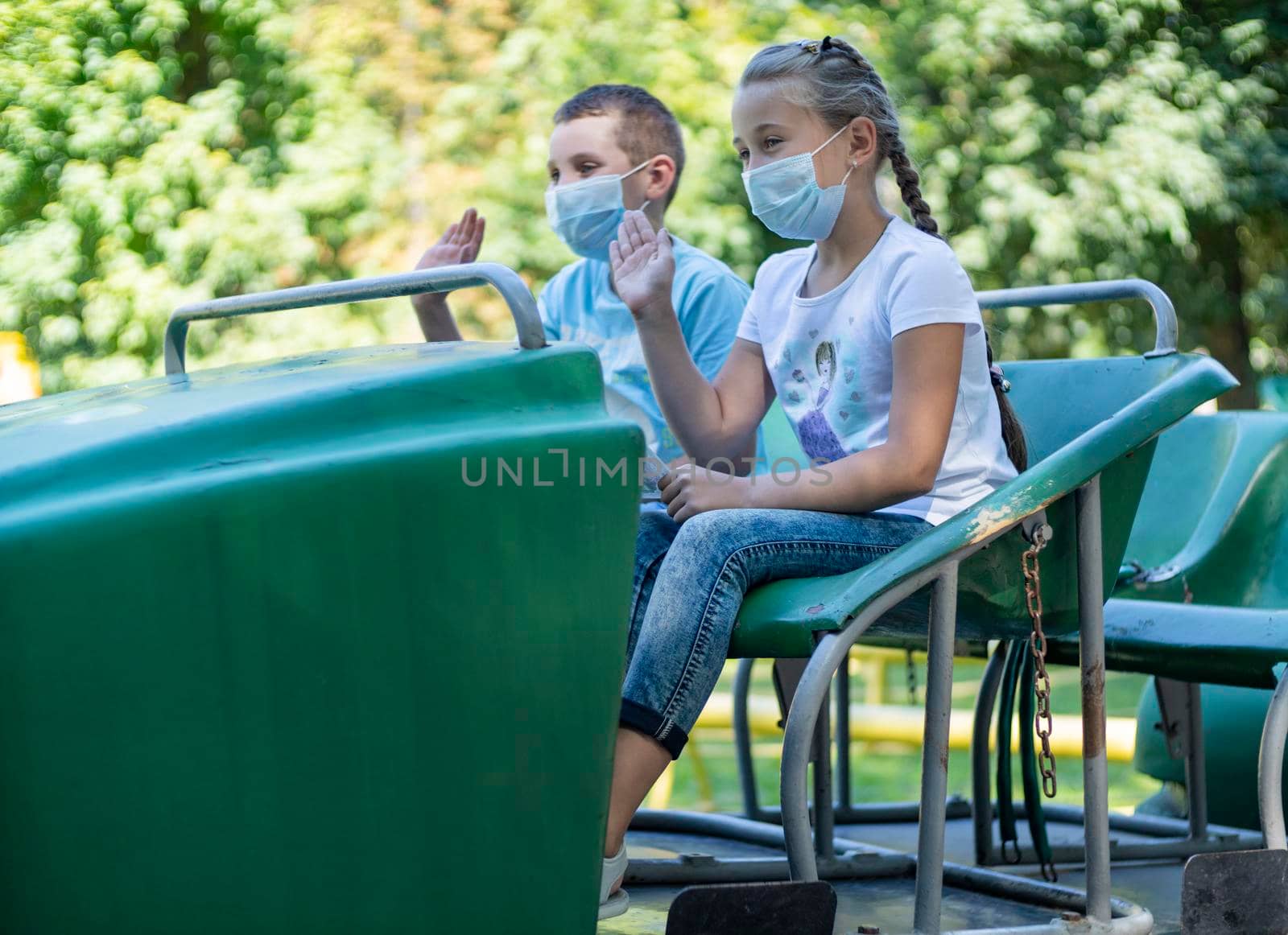 children in medical masks ride an attraction train