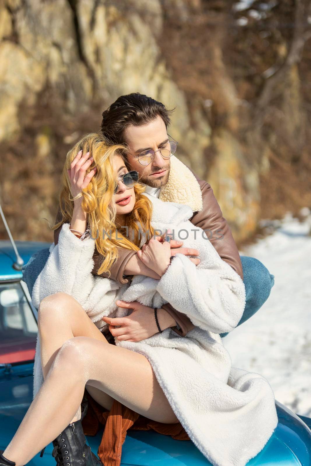 young couple in sun glasses sits on the hood of a retro car