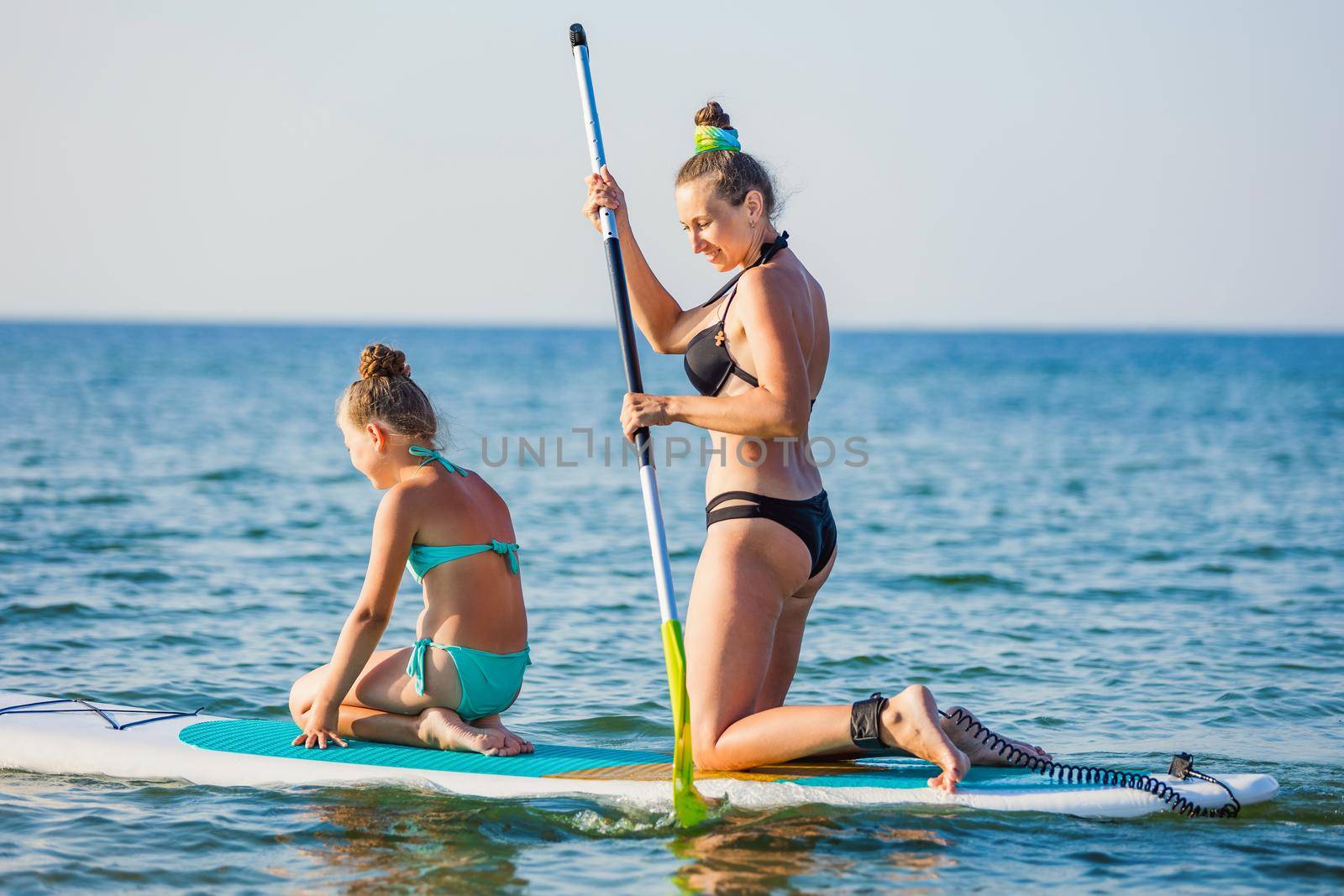 mom and daughter float on the water on a big board