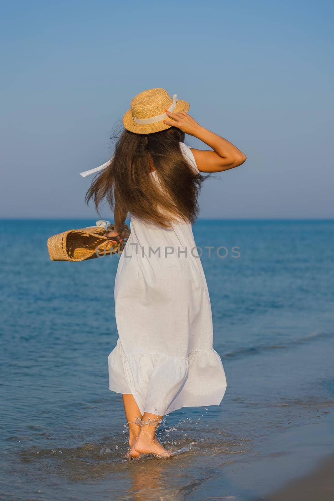 woman in a hat and with a basket in her hands is walking on the beach