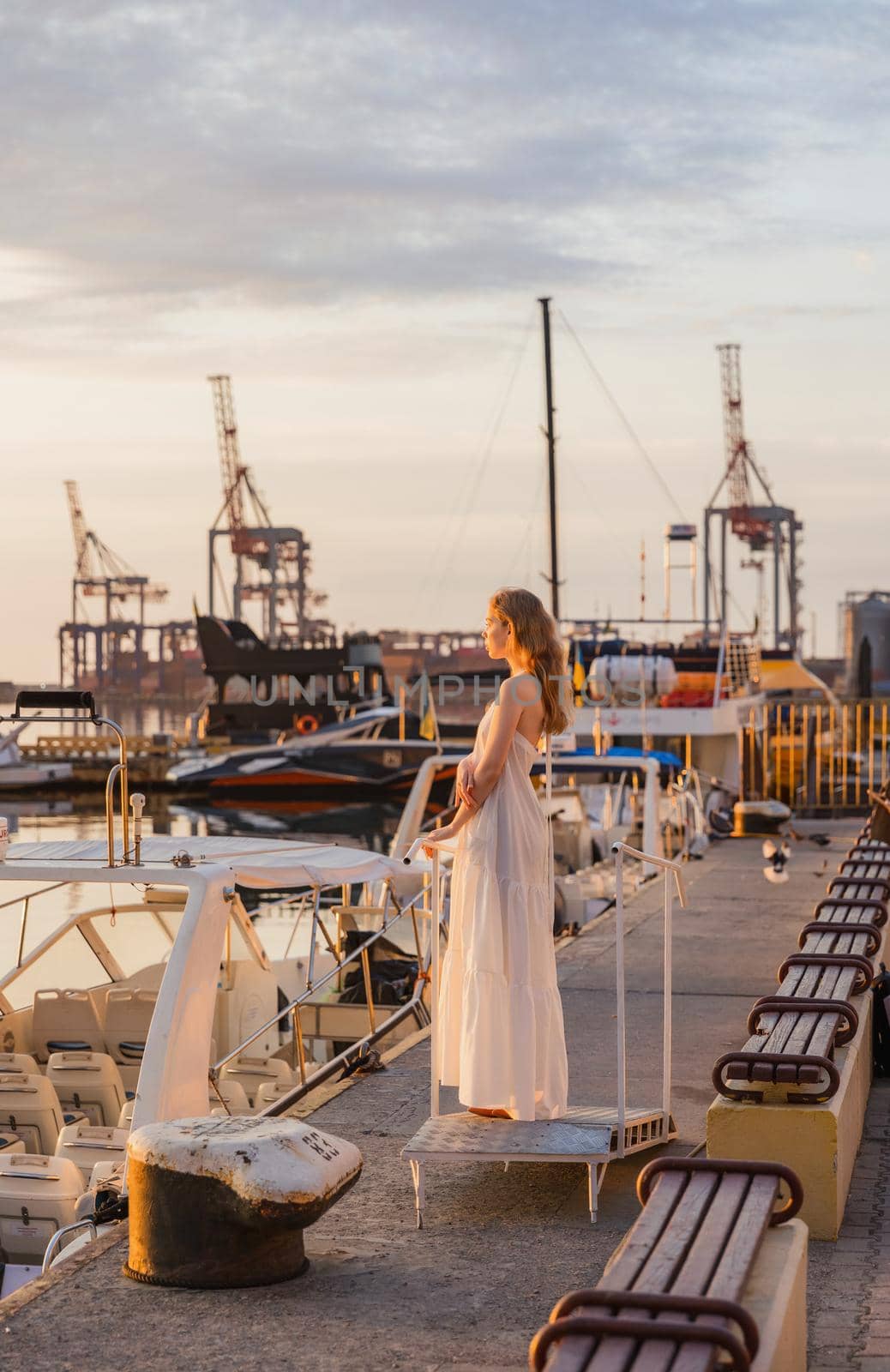 a girl in a white dress stands on the pier against the background of the sea