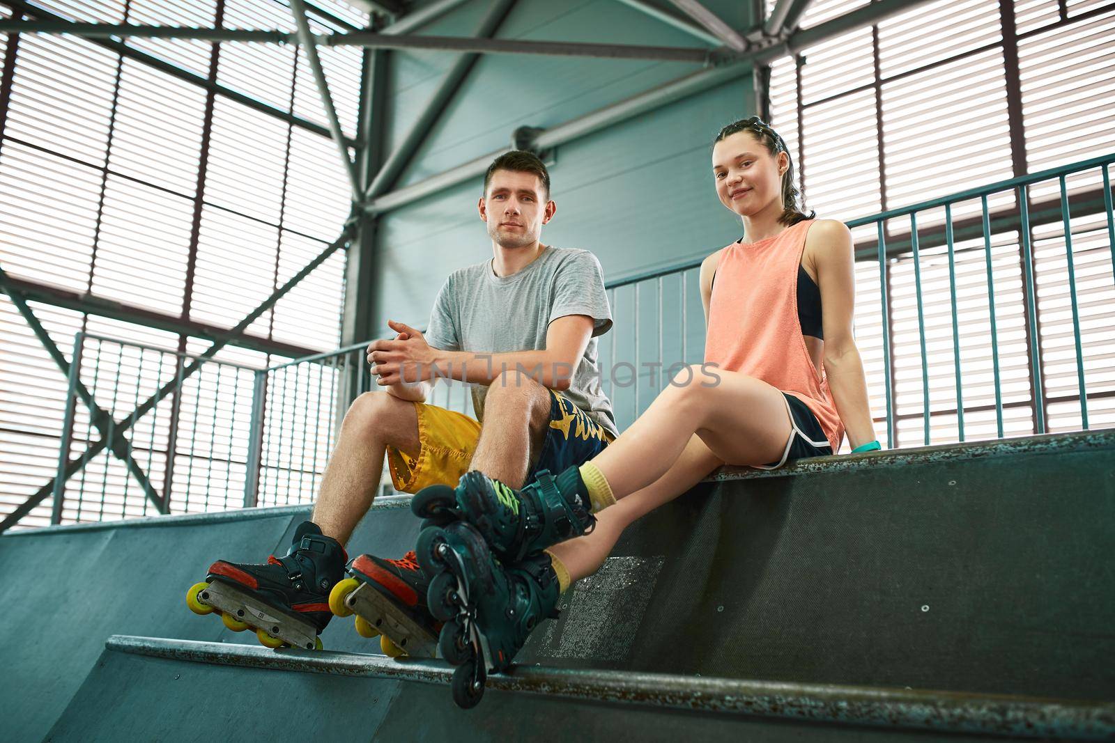 Young man and woman having fun on roller skates in skate park. Extreme sport competition. Indoors skate park equipment. Hobby