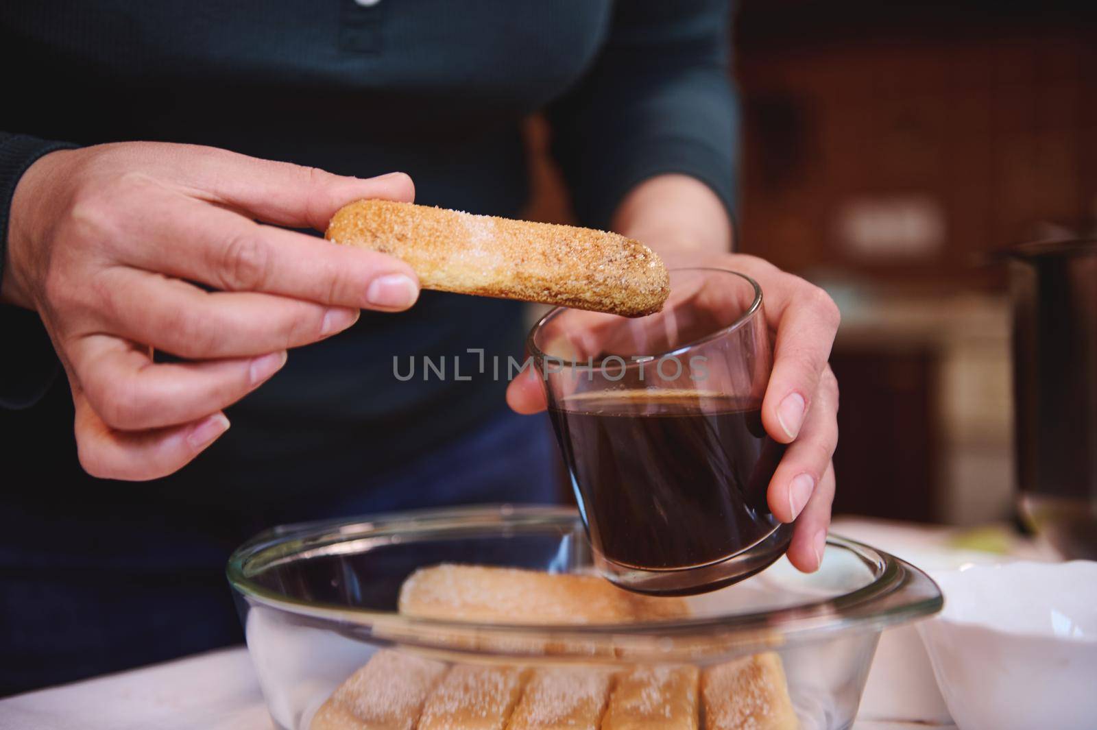 Details: confectioner hands dipping ladyfinger biscuit cookies into a glass of strong sweet espresso coffee. Step-by-step recipe for making traditional Italian dessert Tiramisu at home