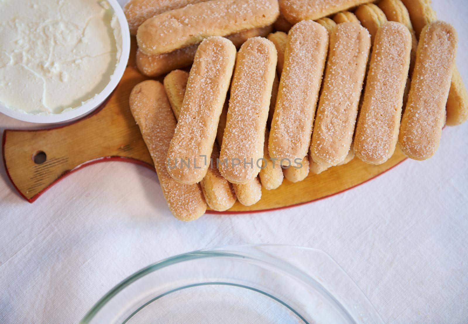 Flat lay composition of savoiardi biscuit cookies on a wooden board and a bowl with mascarpone cheese for The Italian dessert Tiramisu. Copy ad space for text. Step-by-step recipe