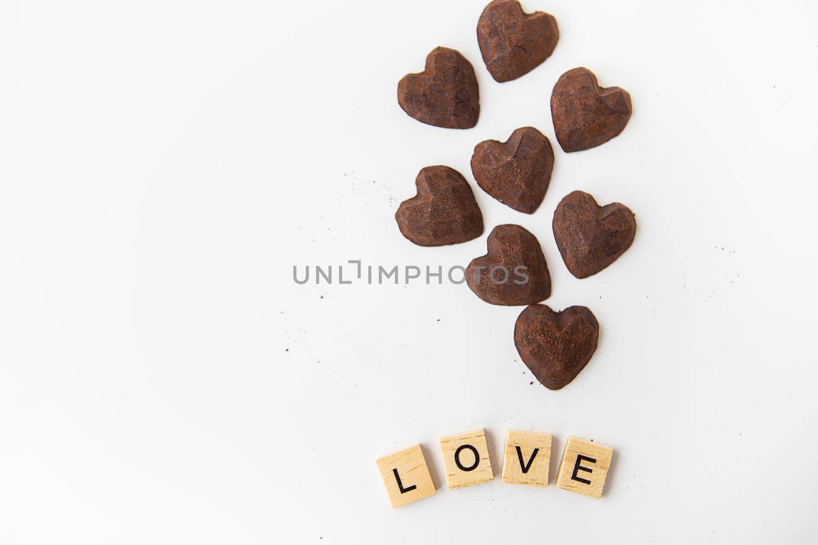 Truffle chocolate candies in the form of a heart on a white background. Inscription love made of wood letters. Place for an inscription