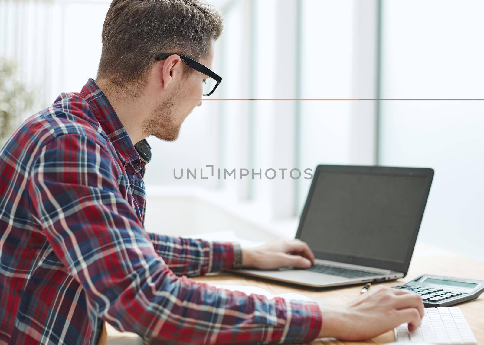 Back view of businessman sitting in front of laptop screen. Man typing on a modern laptop in an office. Young student typing on computer sitting at wooden table. by Prosto
