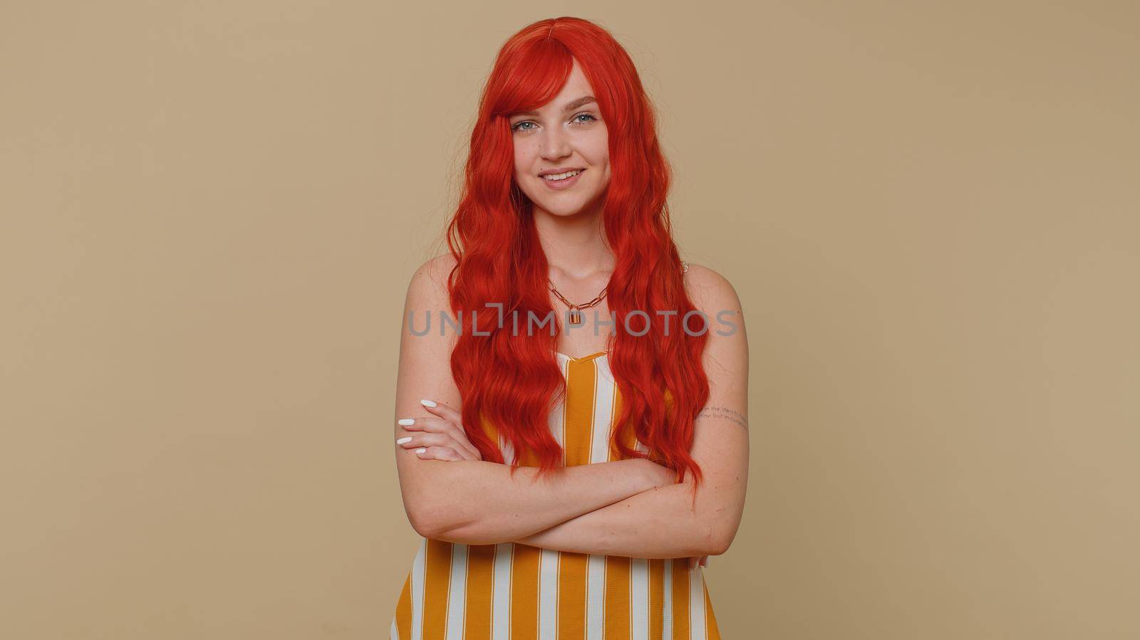 Cheerful lovely redhead adult woman in striped tank top smiling and looking at camera. Young fashion model girl with gray eyes indoors studio shot isolated on beige background. Female nature beauty
