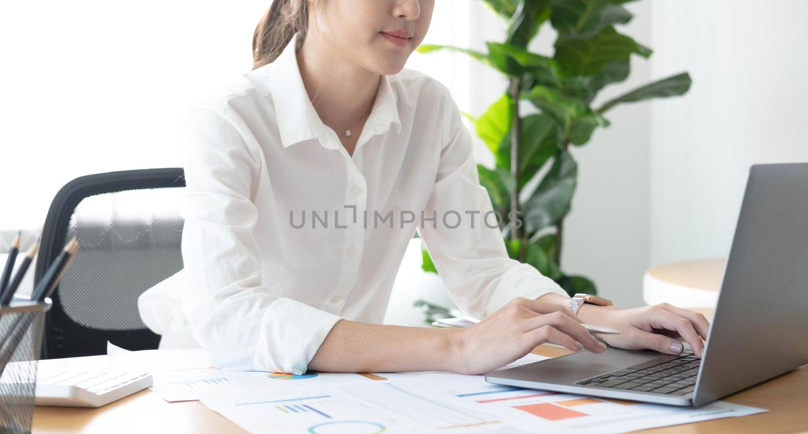 Young Asian businesswoman is happy to work at the modern office using a laptop computer..