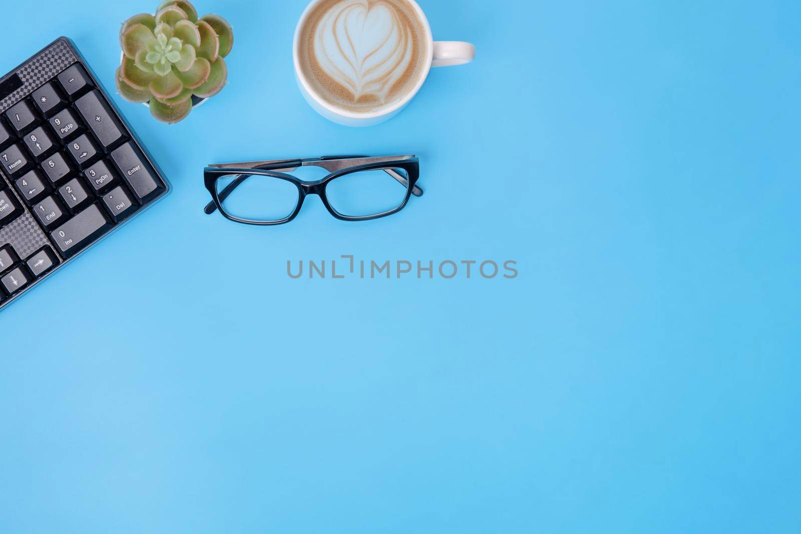 Black keyboard, coffee, glasses, plant on blue background. workplace. Space for text. The financial checks by Iryna_Melnyk