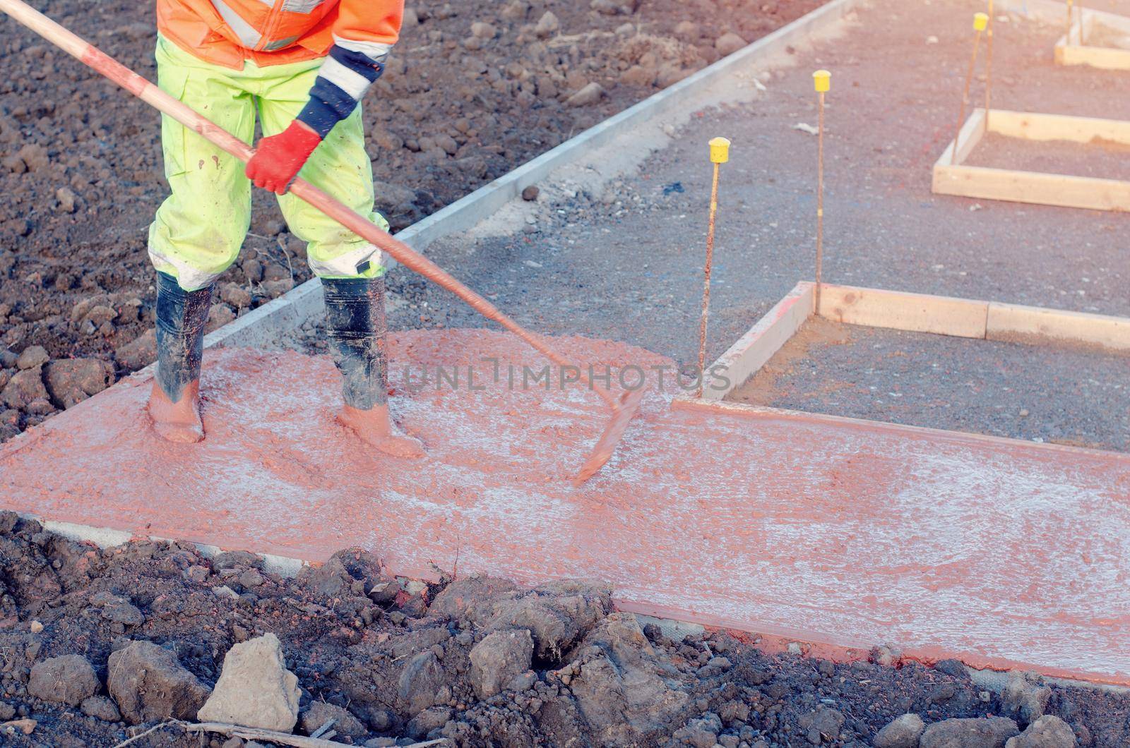 Concreter spreading poured concrete with a rake or spazzle A construction worker is levelling tinted concrete in formwork