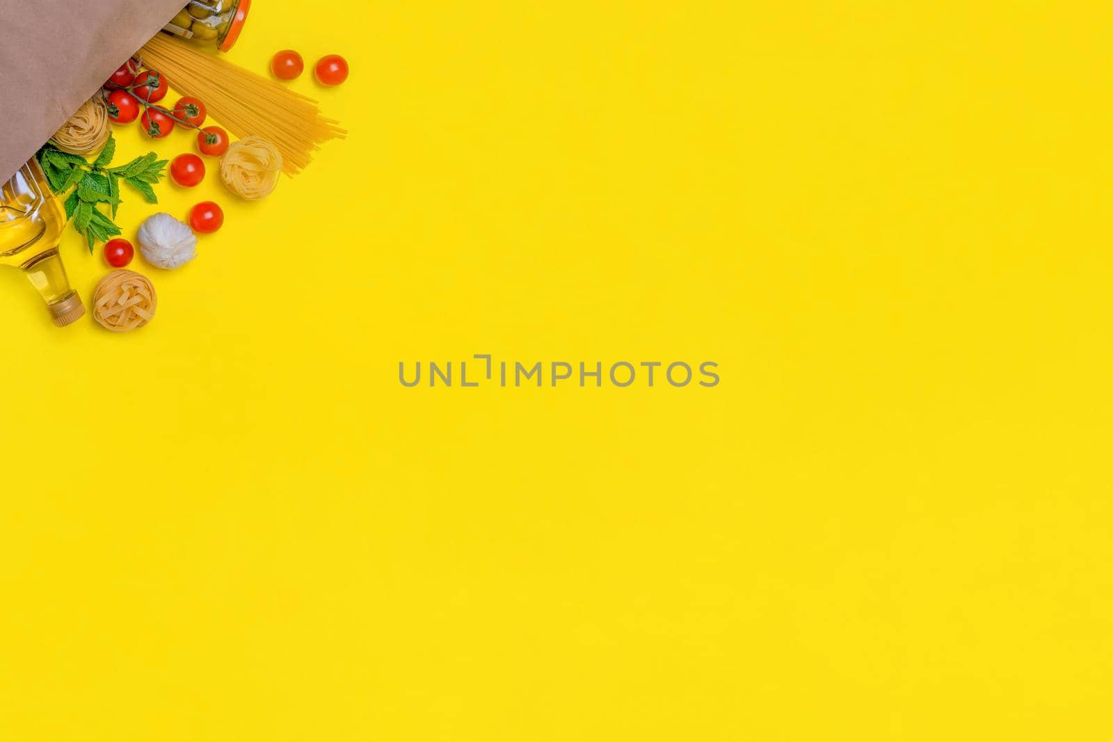 Olive oil, pasta, tagliatelle, olives, egg, cherry tomatoes, garlic in a paper bag on yellow background by Iryna_Melnyk