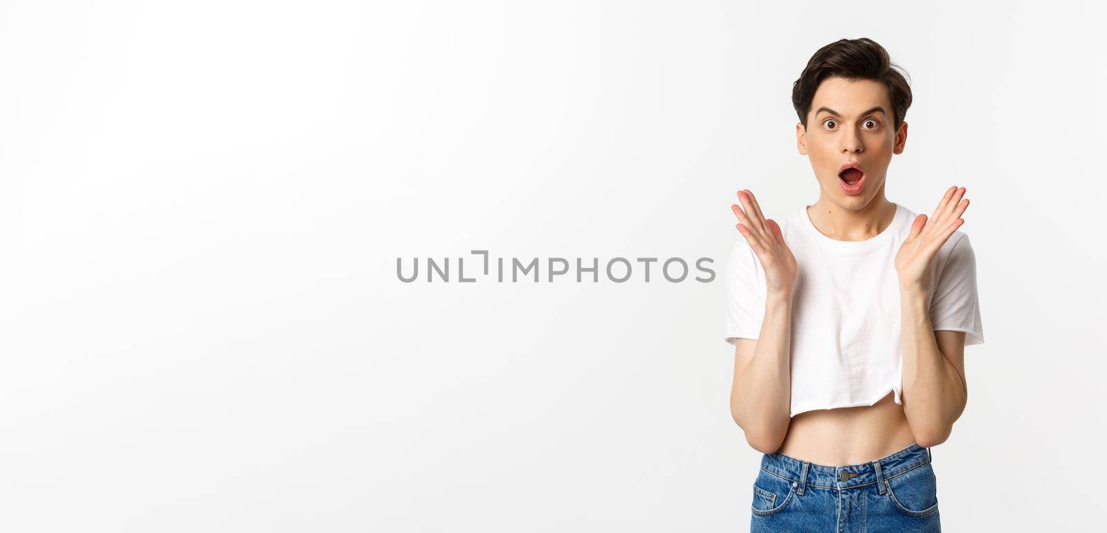 Lgbtq and pride concept. Image of surprised queer guy clap hands and looking in awe at camera, standing in crop top against white background by Benzoix