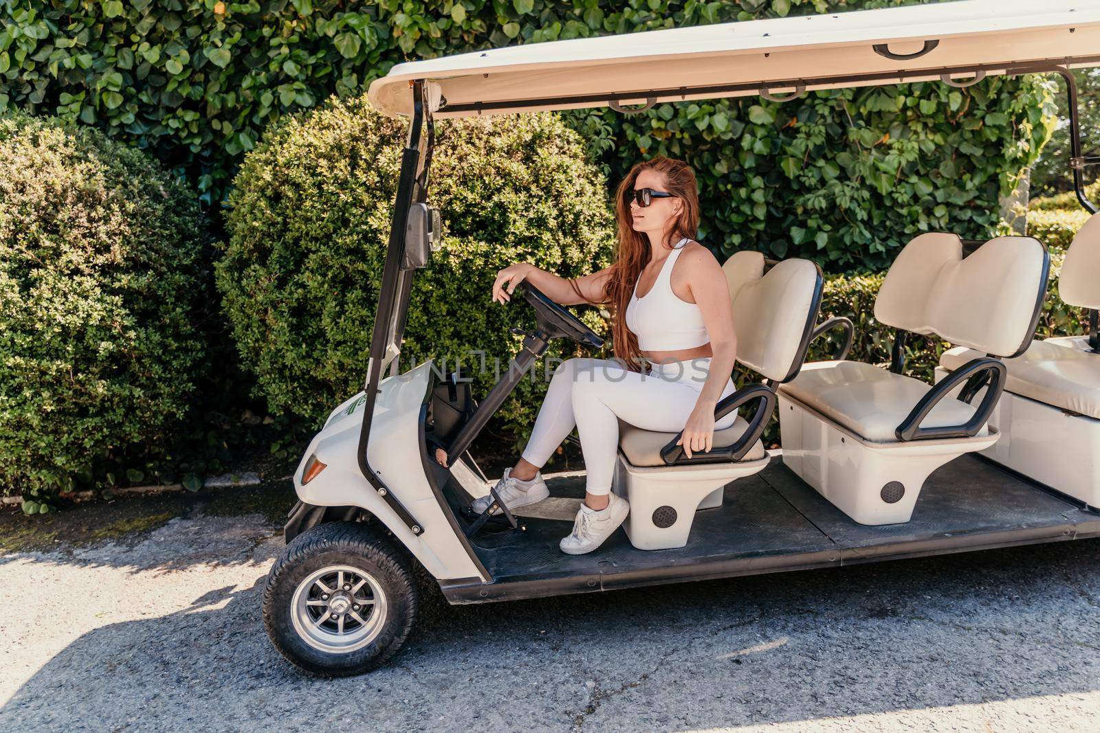 A middle-aged woman is driving a car for transporting tourists. Electric car, Tourist bus. Car for transporting people around the hotel, park, golf club by Matiunina