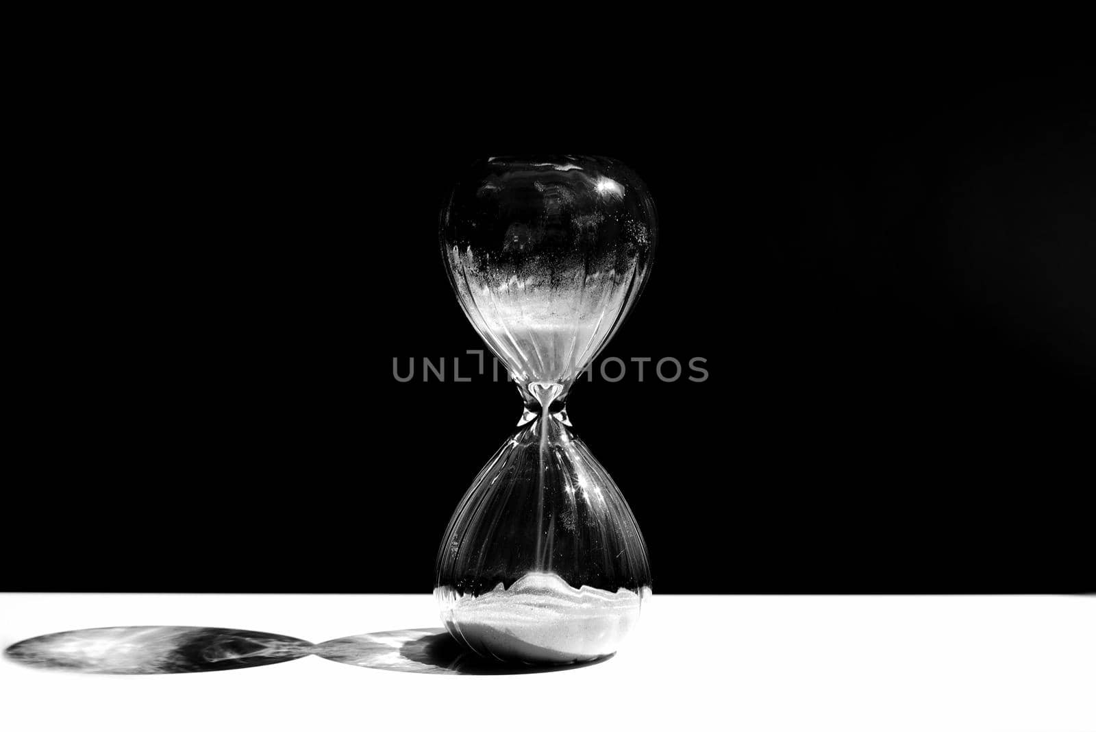 Hourglass, sandglass with sand on a black background with a streak of white light and a shadow