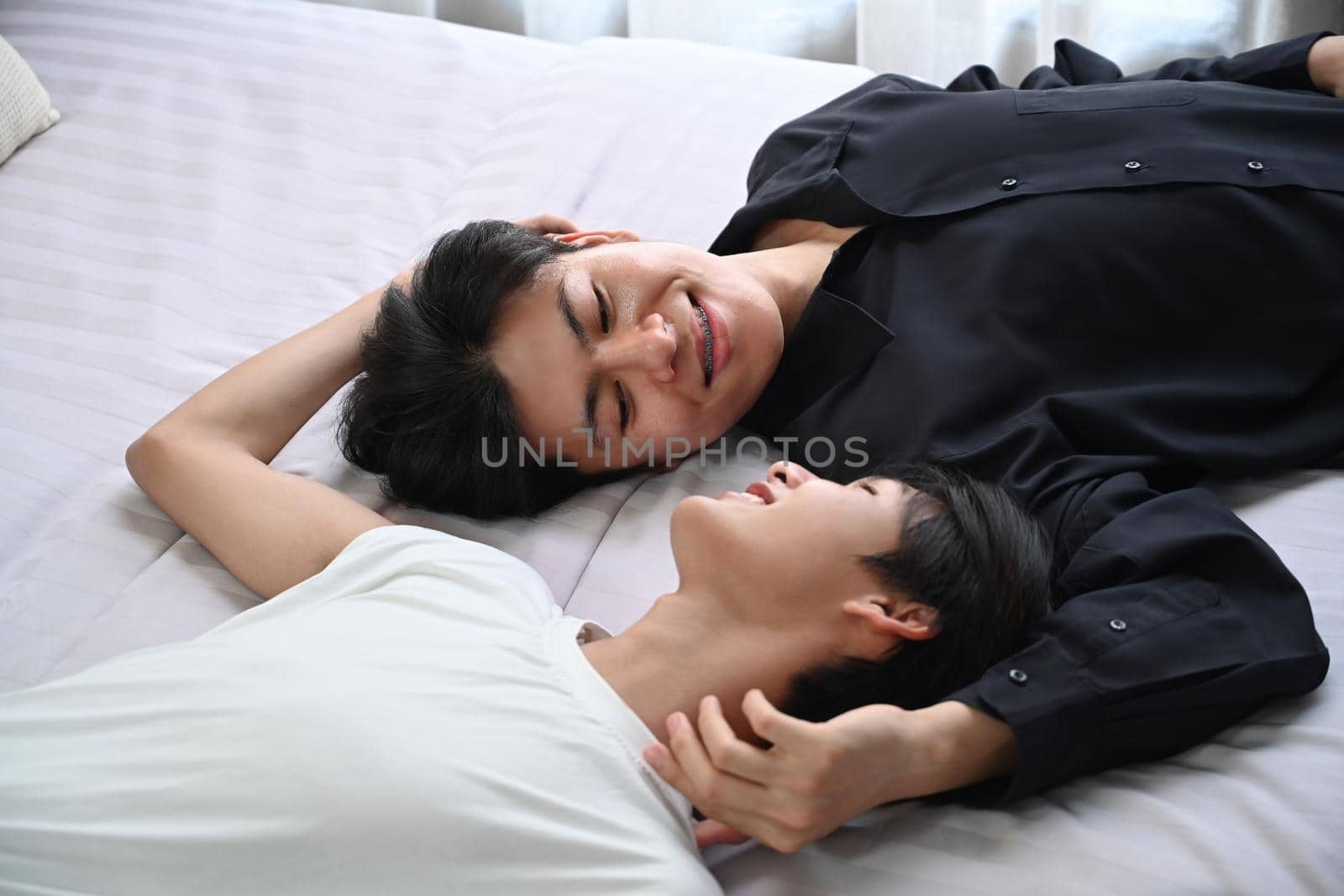 Loving homosexual couple lying down on bed, spending time together at home. LGBT, pride, relationships and equality concept.