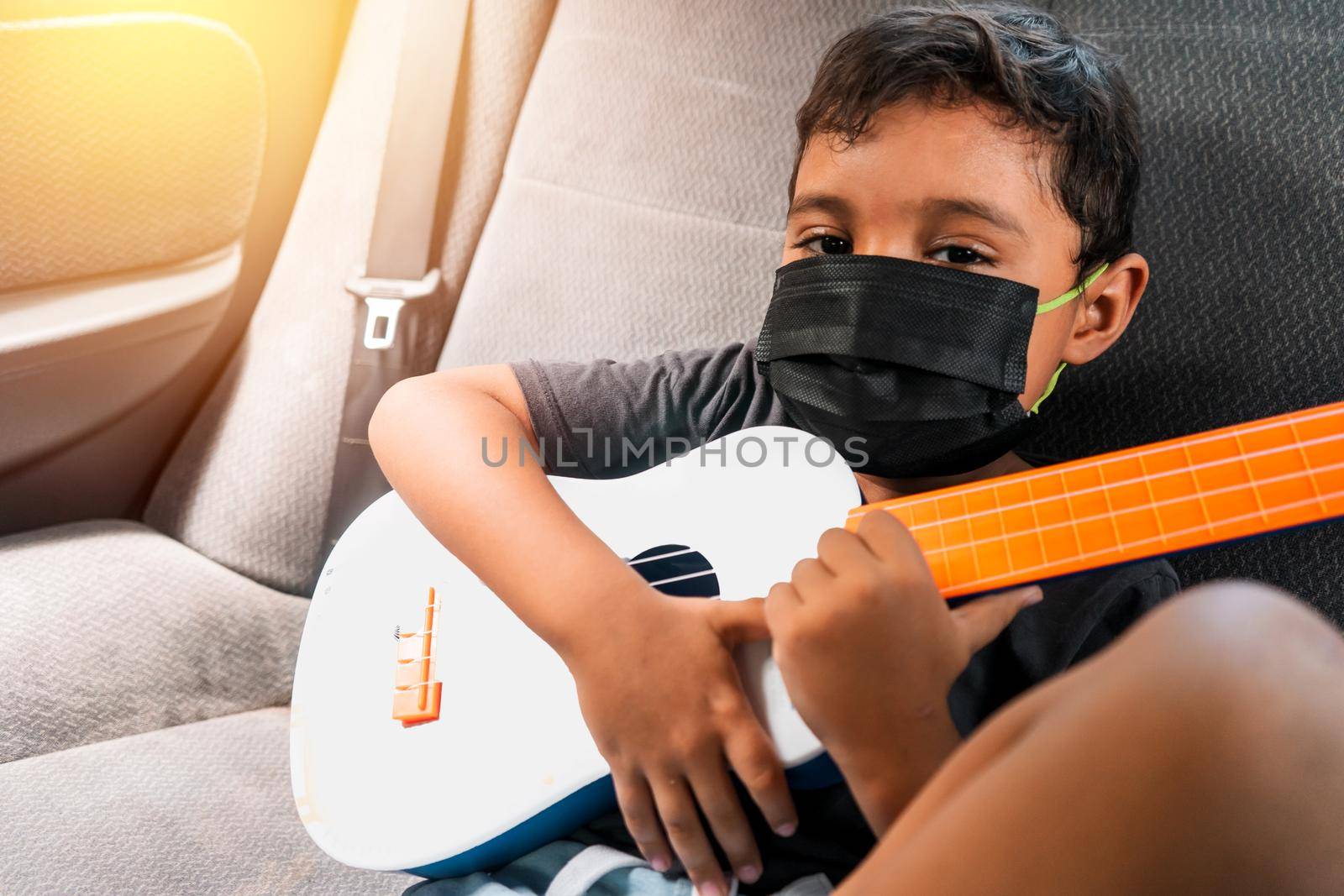 Latin boy in the back seat of a car with a ukulele by cfalvarez