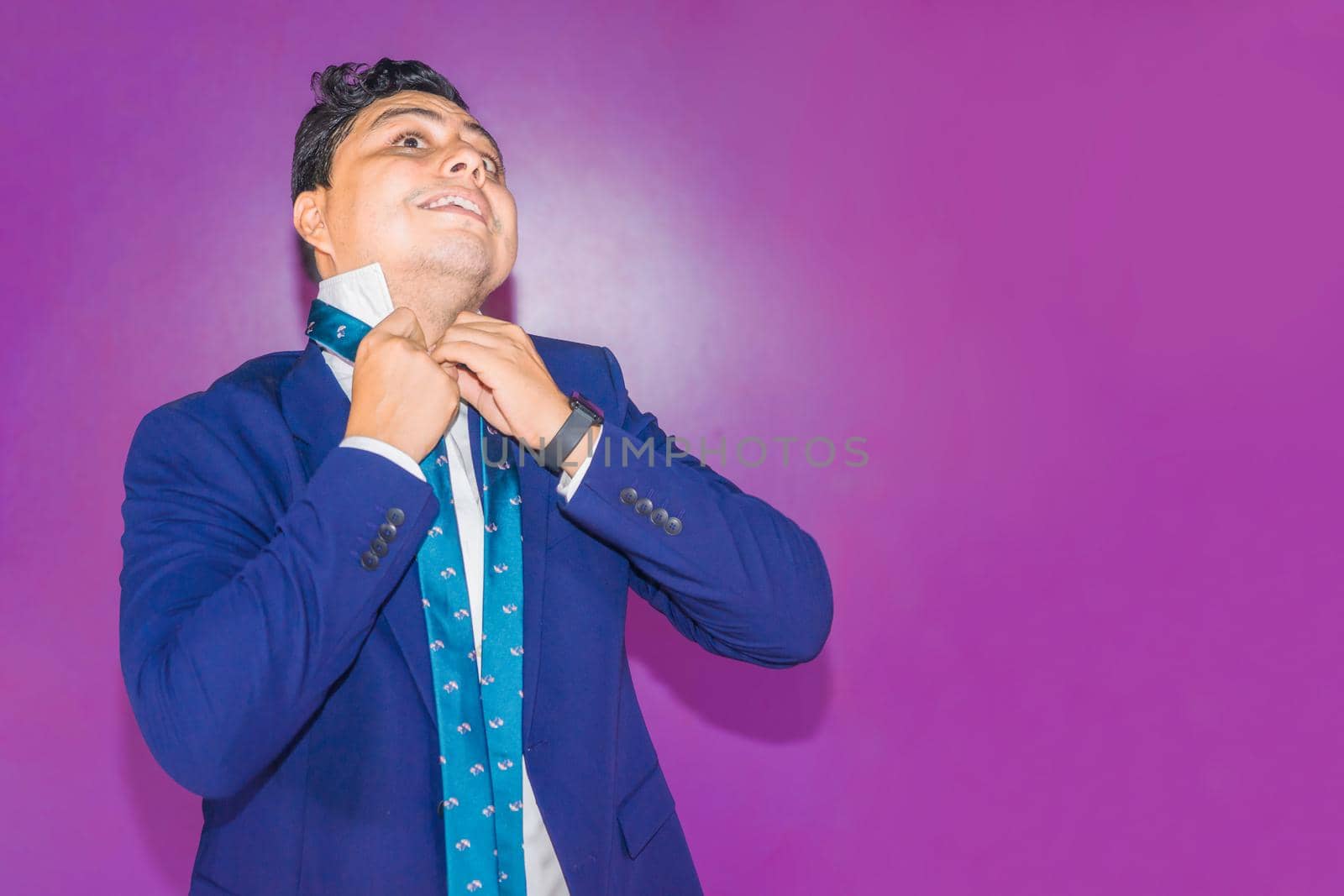 Latin Nicaraguan man in a blue suit having trouble tying his tie knot on a flat purple background