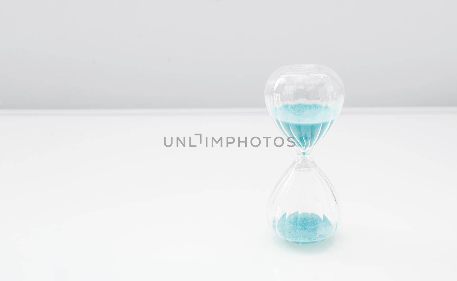 Hourglass on bright light, sandglass with blue sand on white background