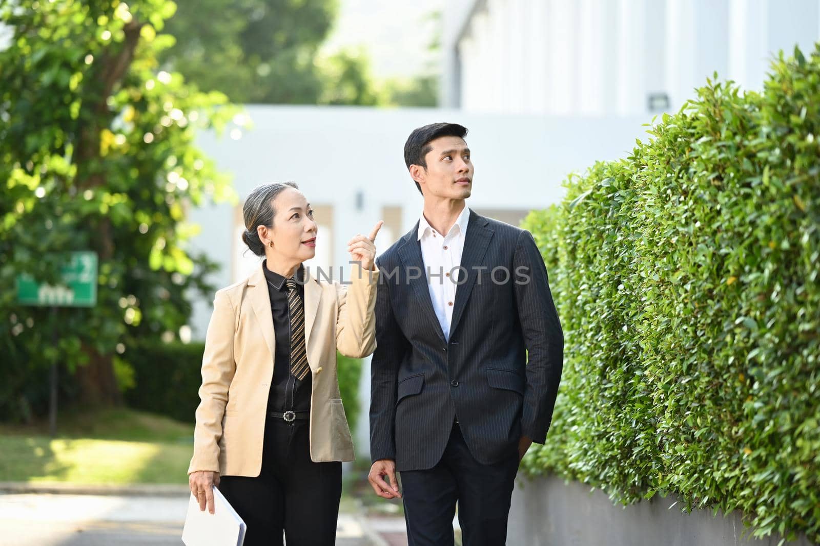 Two business people in formalwear discussing business while walking on street in modern city.